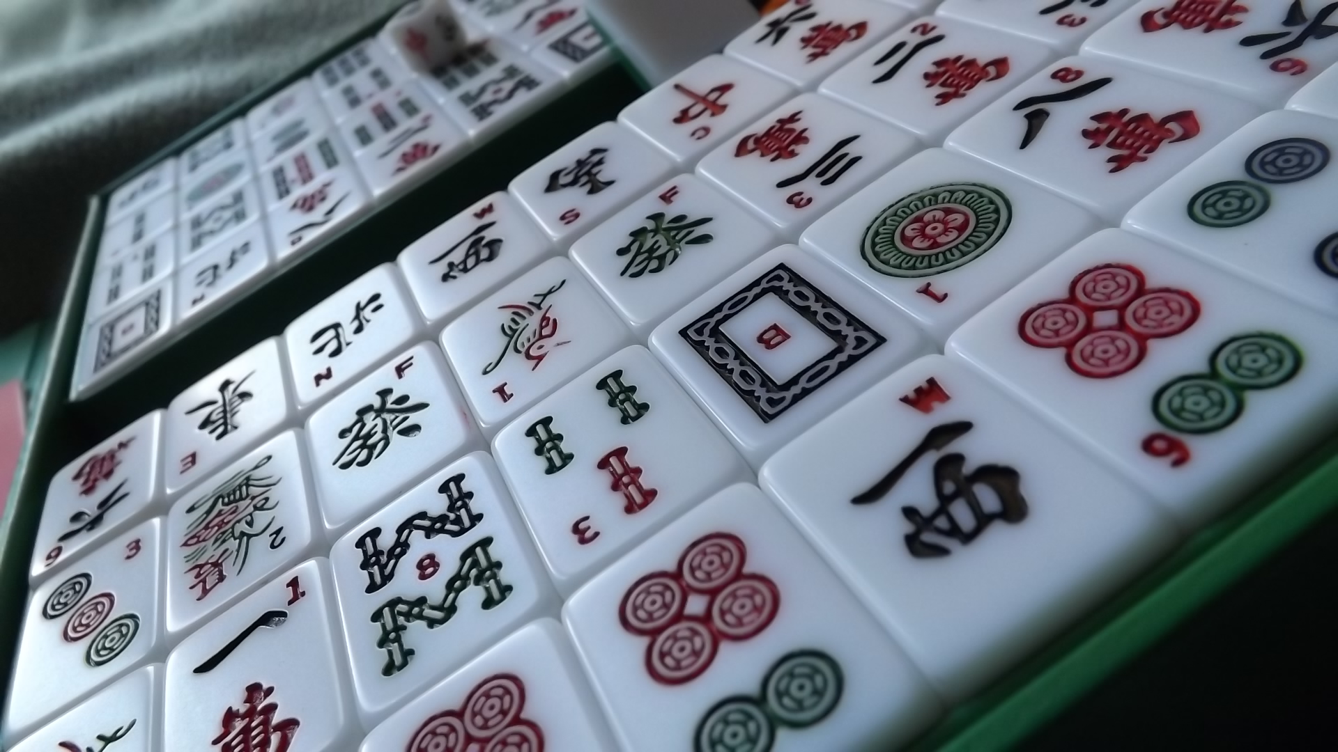 Glossy ivory mahjong tiles with red and green markings, photographed at an angle on a dark surface